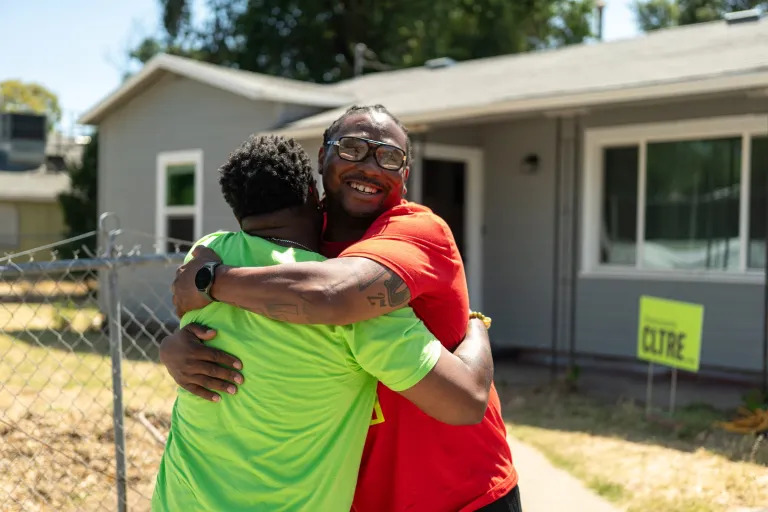 A person in a green shirt and a person in an orange shirt hug