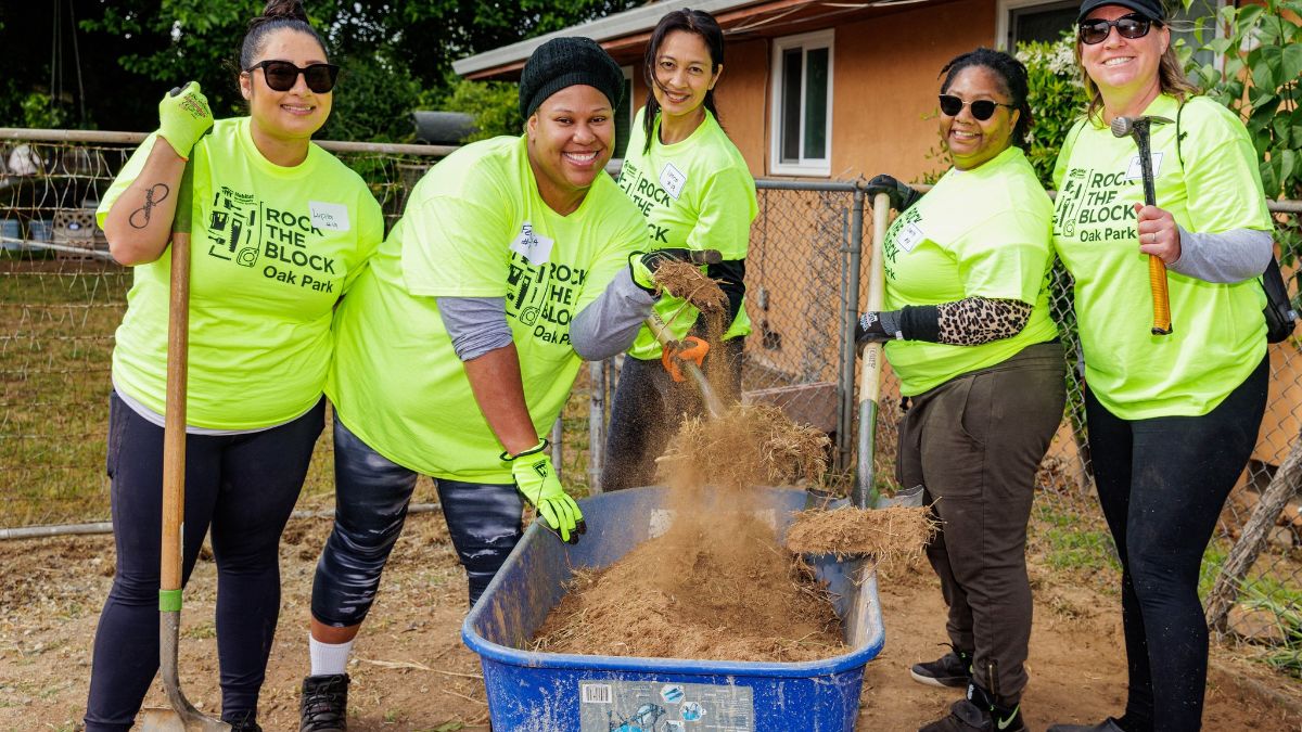 A group of volunteers shoveling dried grass into a wastebin