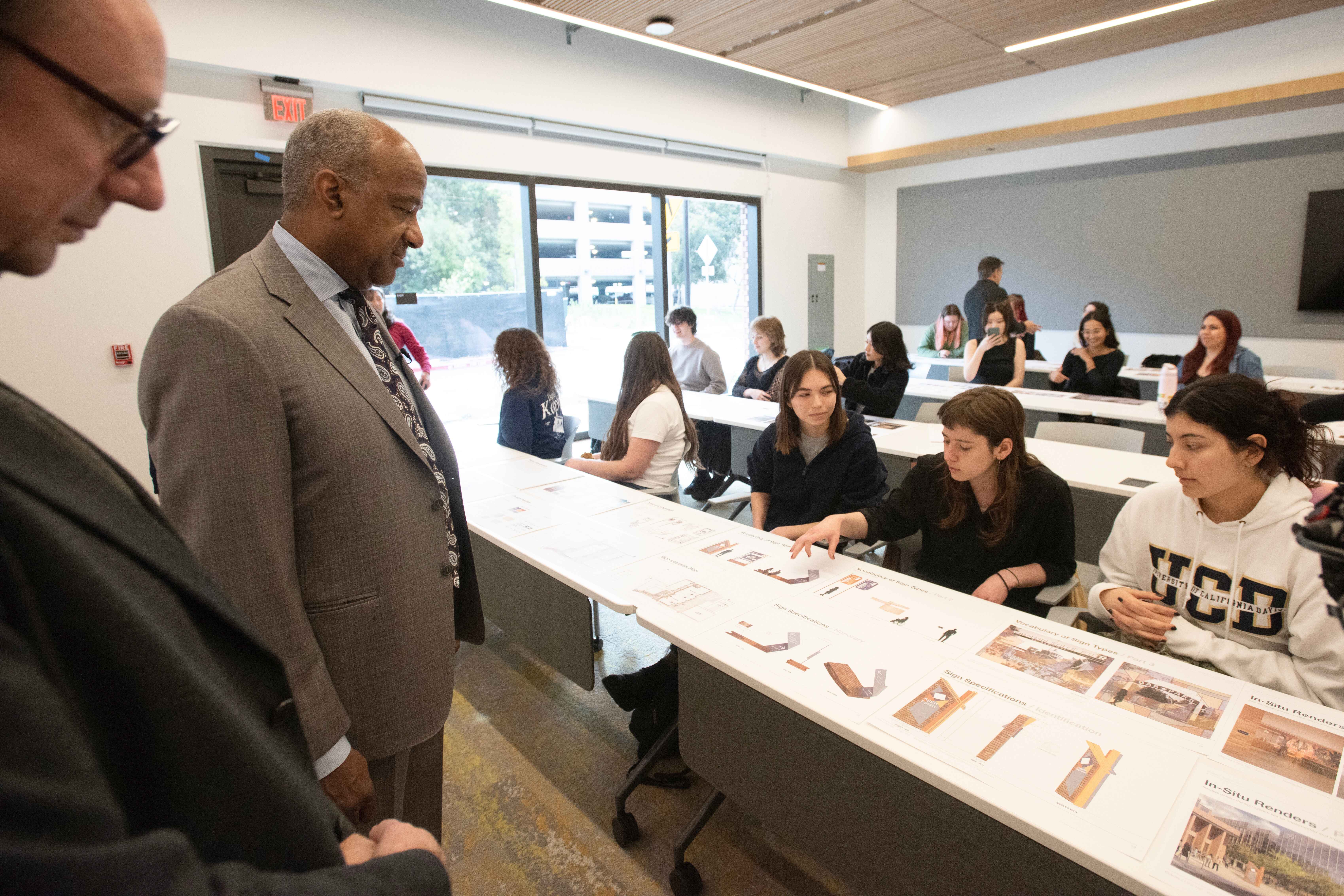 A group of students seated as they explain their poster to a man standing