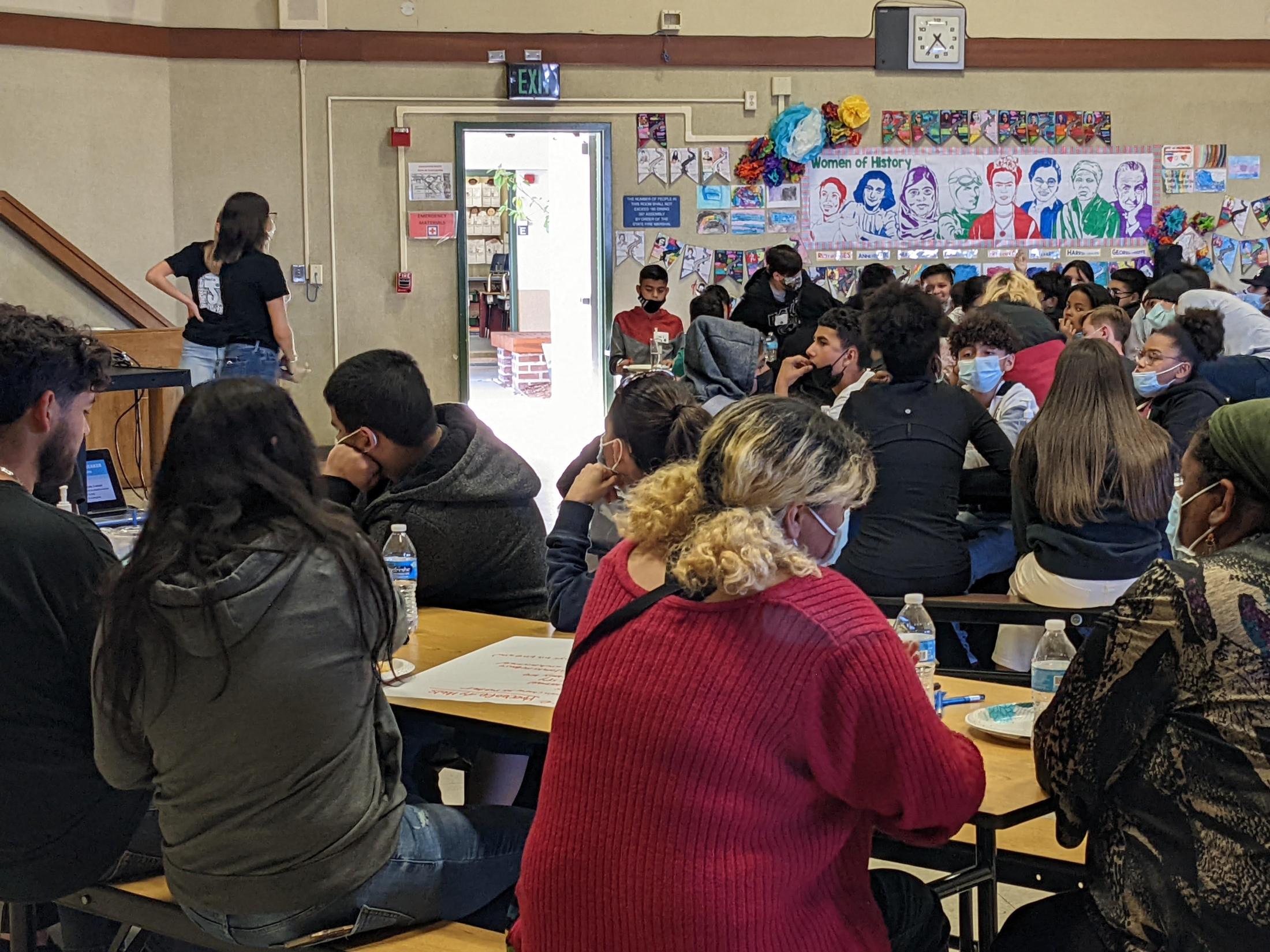 Students sit in a multiple purpose room.