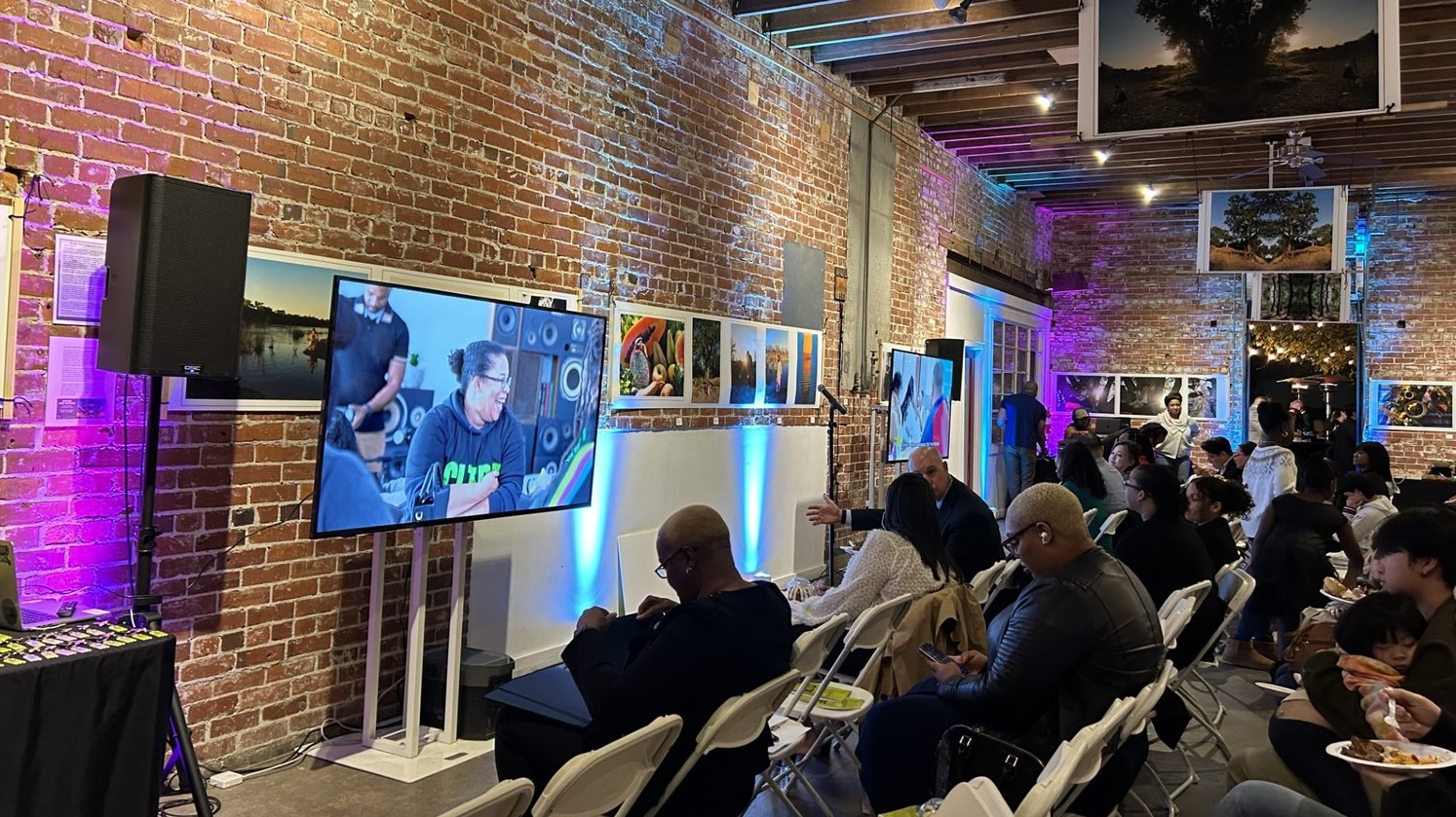 A group of people gather watching a speaker on screens