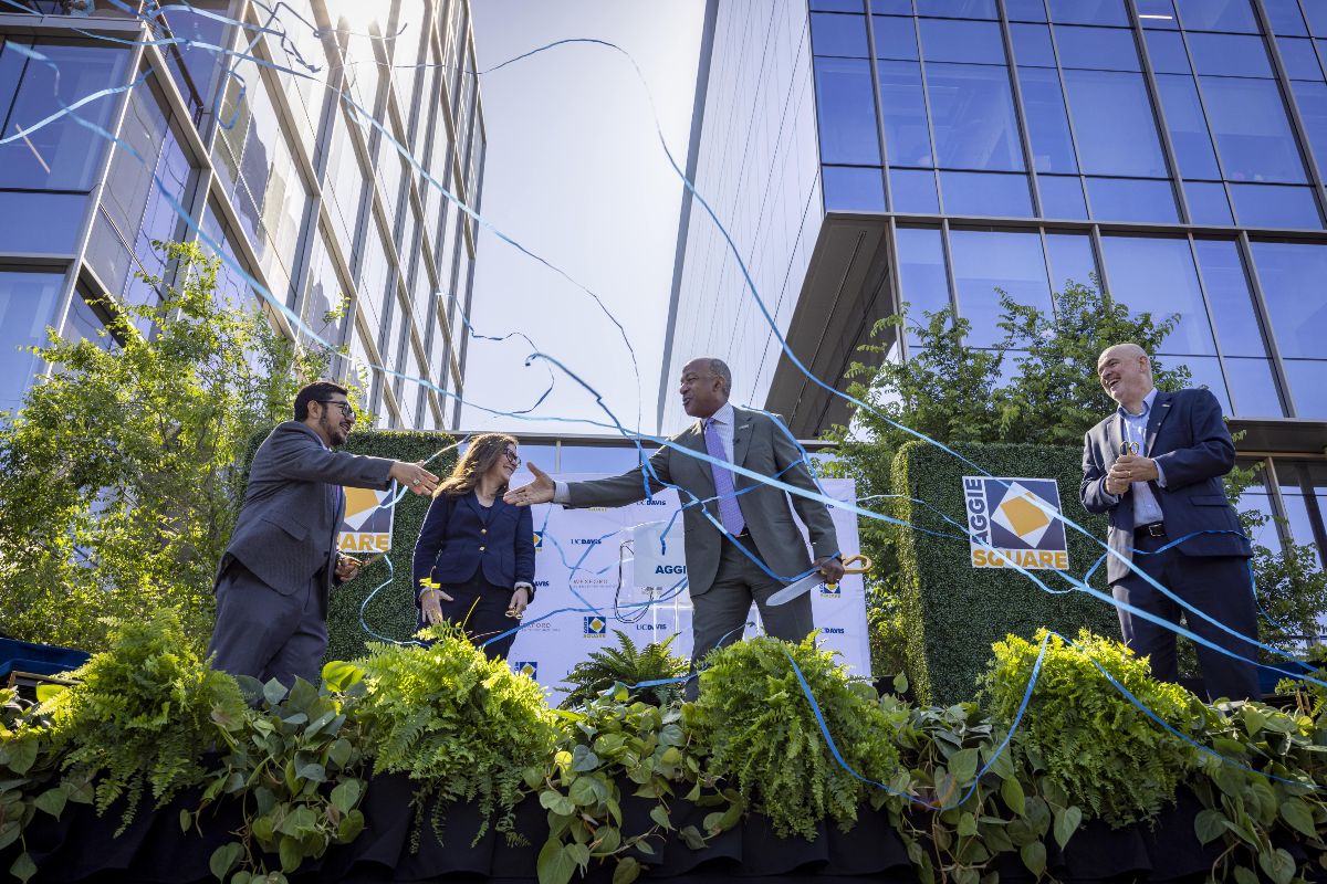 Leaders from UC Davis, the city of Sacramento and Wexford Science & Technology stand on a podium in front of a building shaking hands after cutting a ceremonial ribbon