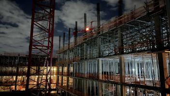 Image of the Aggie Square construction site at night. The bright orange light on a crane shines with the Whiting-Turner logo. 