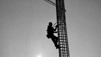 Black and white image of the silhouette of a construction worker climbing a column grid. 