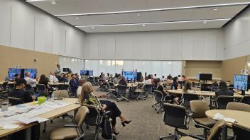 People sit at various tables in a large conference room.