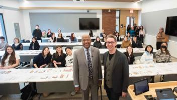 Two men in the front of a classroom posed for a photo with class