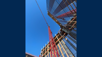 Image from below, looking straight up at a red crane next to a reflective building at UC Davis Aggie Square.