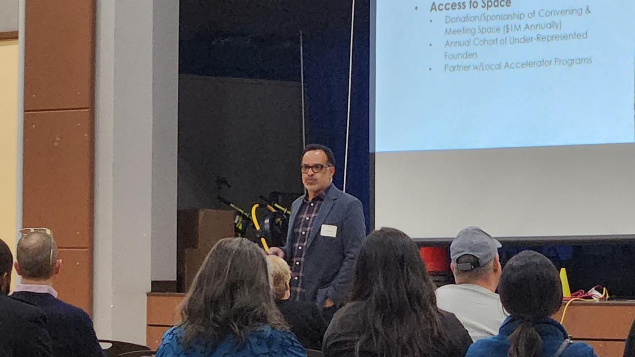 Man standing in front of audience with a presentation behind him