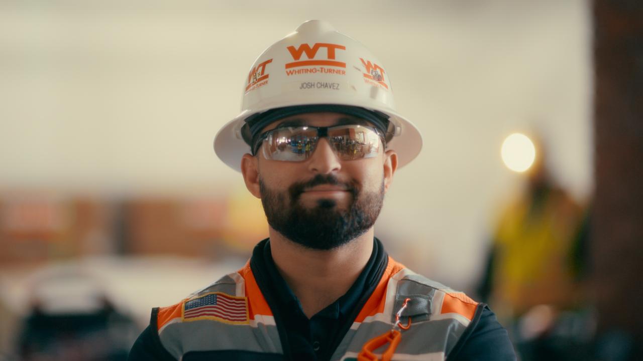 Photo of a bearded construction worker wearing a hard hat and safety vest looking at the camera.