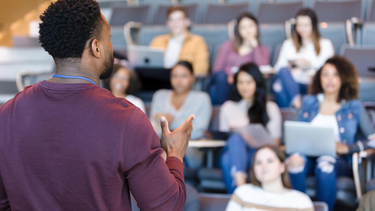 Man with back to camera talking to seated students
