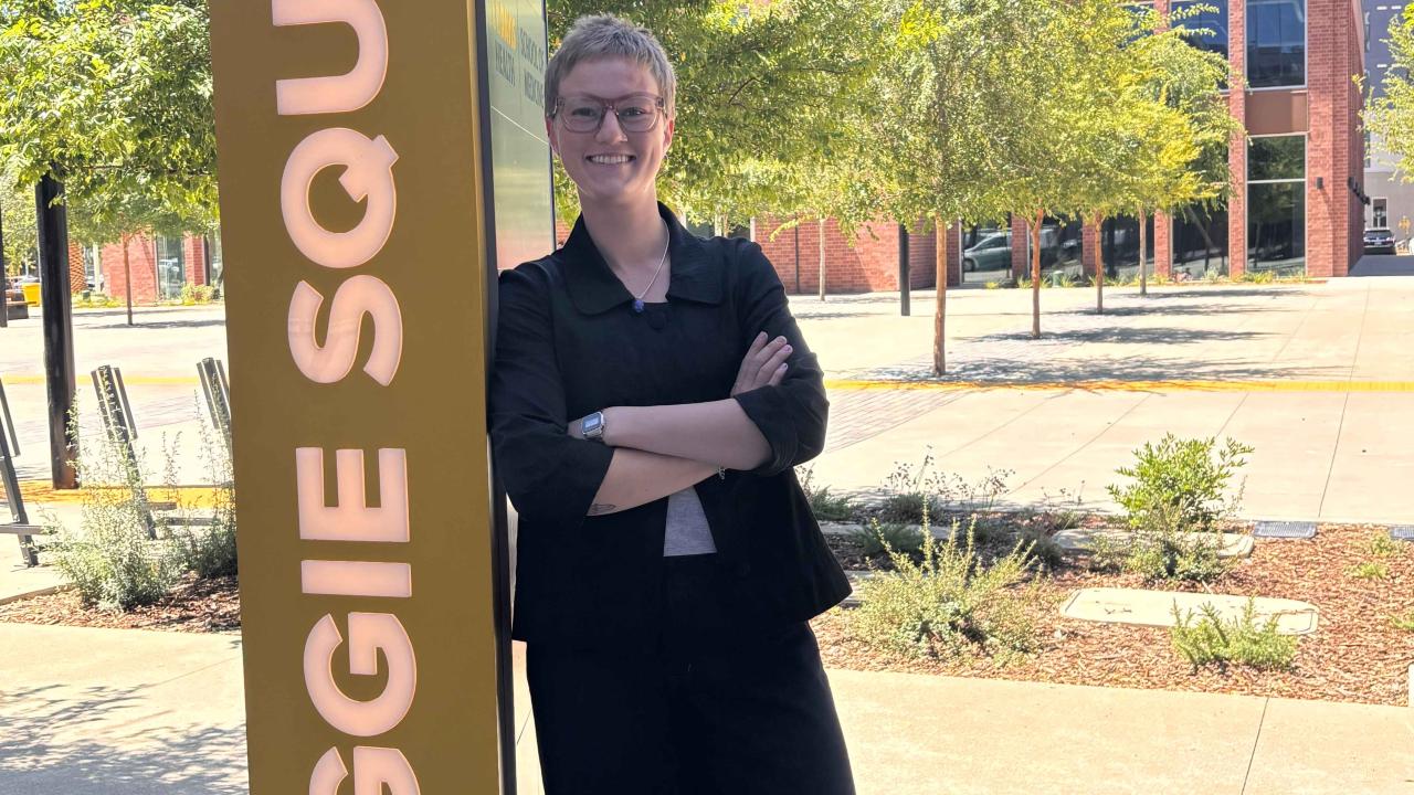Bailey Day leans against a pillar that reads "Aggie Square"