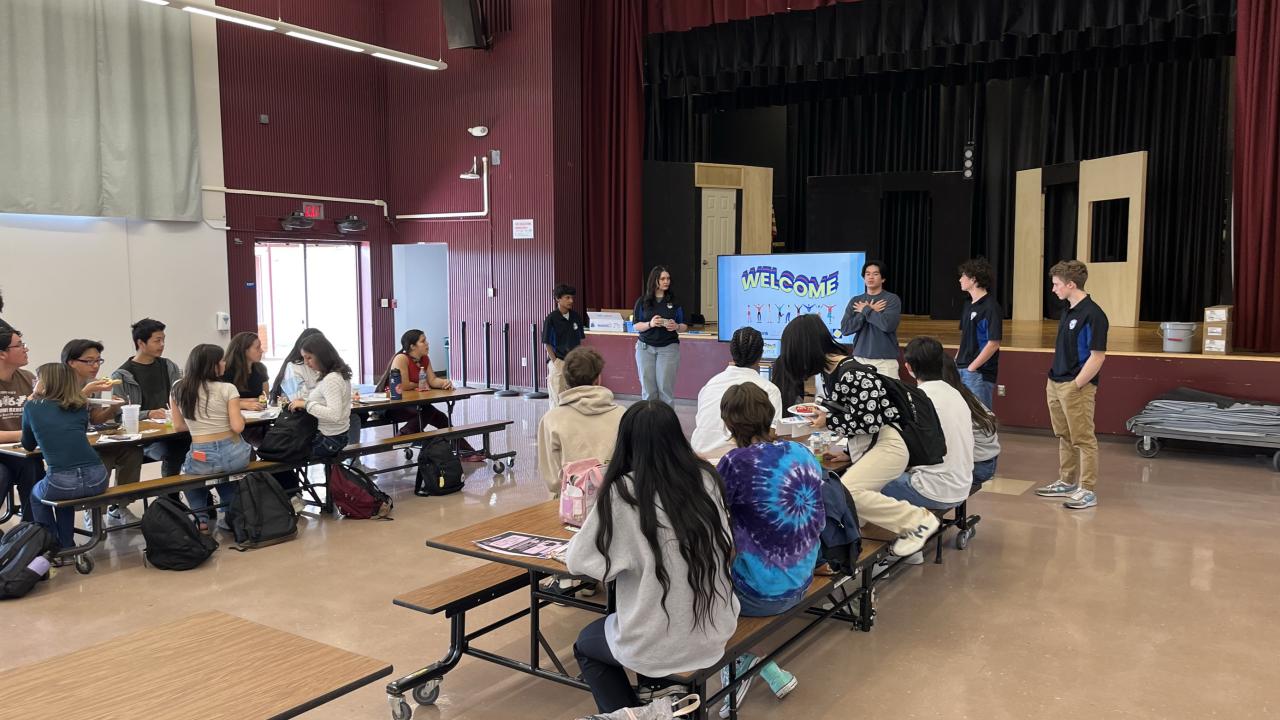 A group of students in a cafeteria listening to a presenter