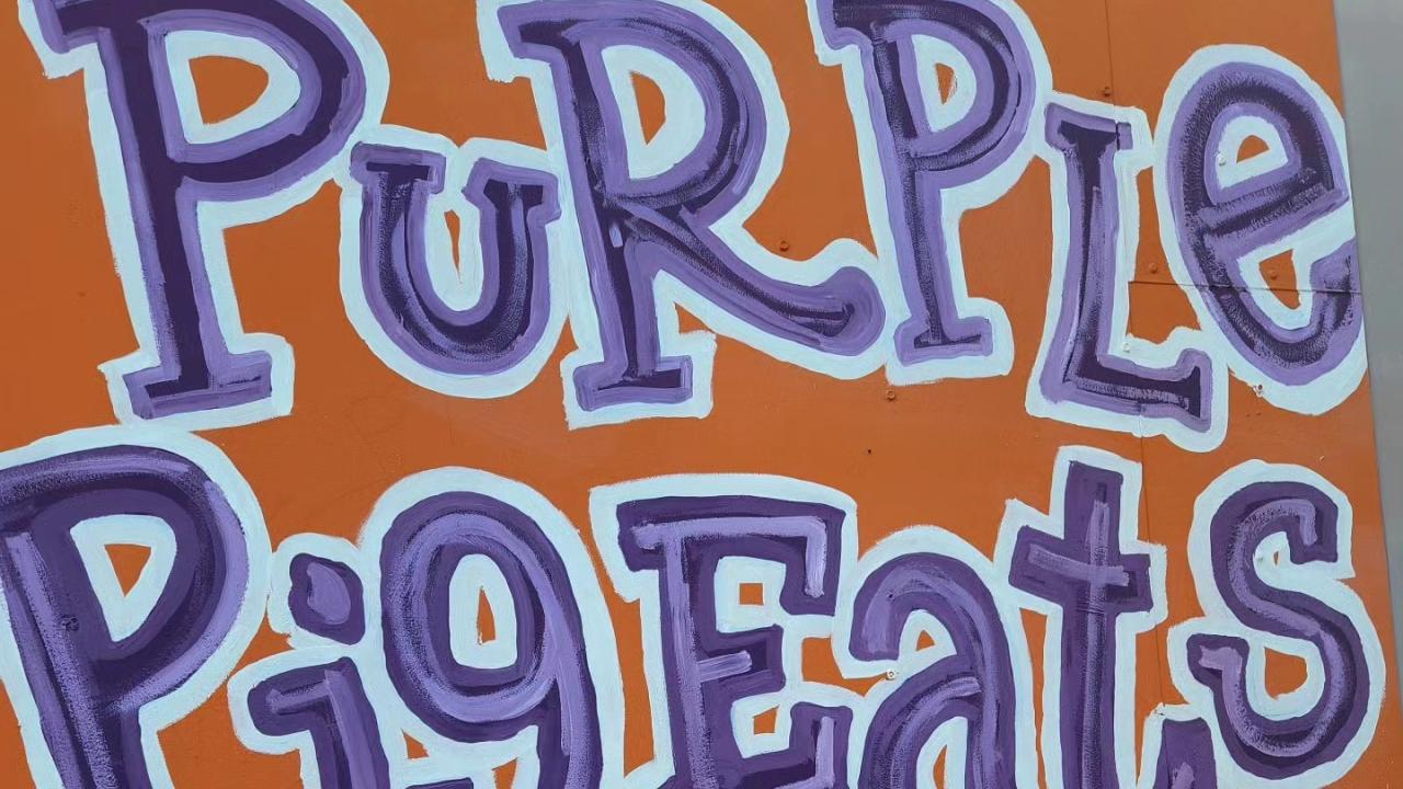 A burger in front of an orange sign with purple text that reads "Purple Pig Eats, Oak Park"