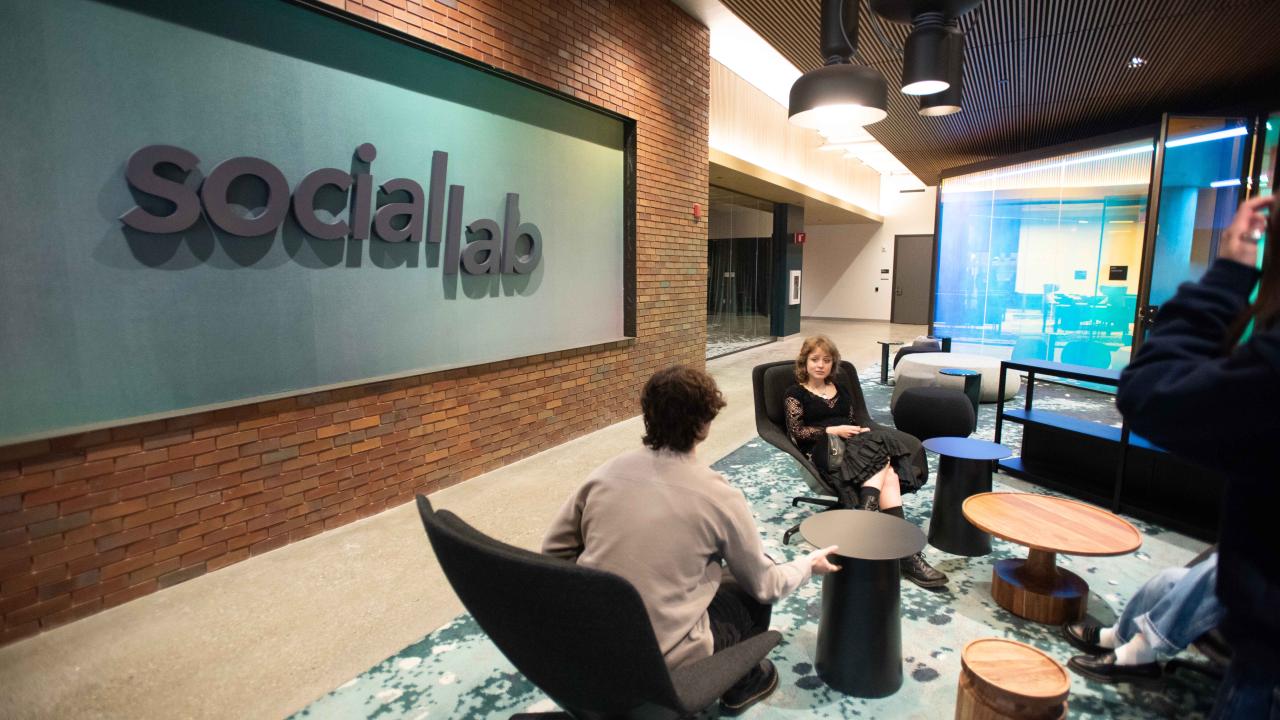 A group of people sit close to a wall with the words "social lab" on it