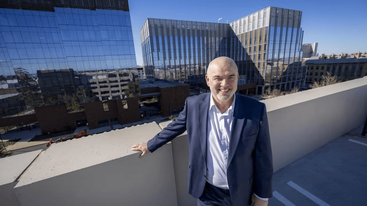 George Baxter poses for photo with Aggie Square buildings in background.