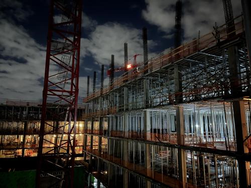 Image of the Aggie Square construction site at night. The bright orange light on a crane shines with the Whiting-Turner logo.