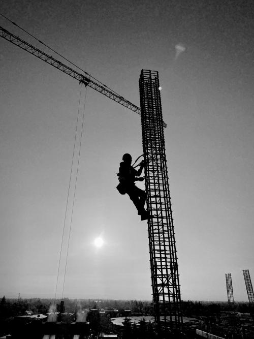 Black and white image of the silhouette of a construction worker climbing a column grid.