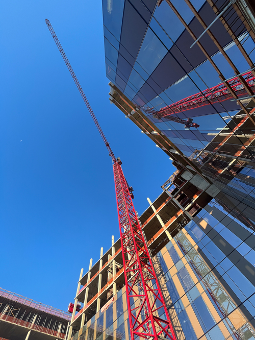 Image from below, looking straight up at a red crane next to a reflective building at UC Davis Aggie Square.
