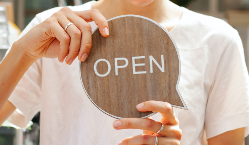 hands holdiing up a wooden sign that says "OPEN"