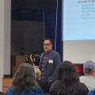 Man standing in front of audience with a presentation behind him