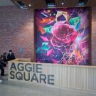 Students mingle next to the reception desk in front a brick wall with a large mural of a flower on it.