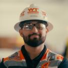 Photo of a bearded construction worker wearing a hard hat and safety vest looking at the camera.