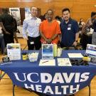 Three people pose for a photo behind a table with the words UC Davis Health
