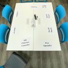 A table with six blue chairs around it and paper on the table with labels of different job occupations