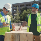 Two construction workers talk together in front of construction